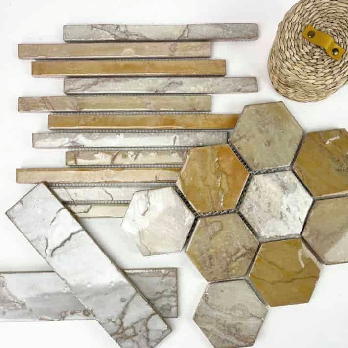 A collection of various stone tiles in different shapes and colors, including hexagonal and rectangular pieces, arranged on a surface with a woven basket.