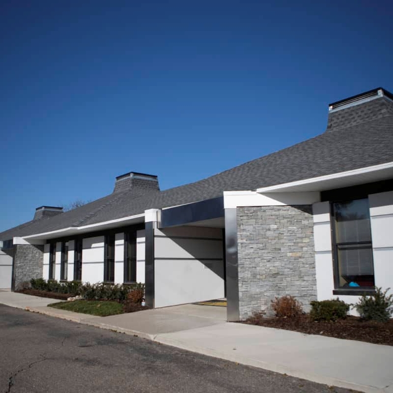 A modern building with a sloped roof, featuring stone accents and a clear blue sky in the background.