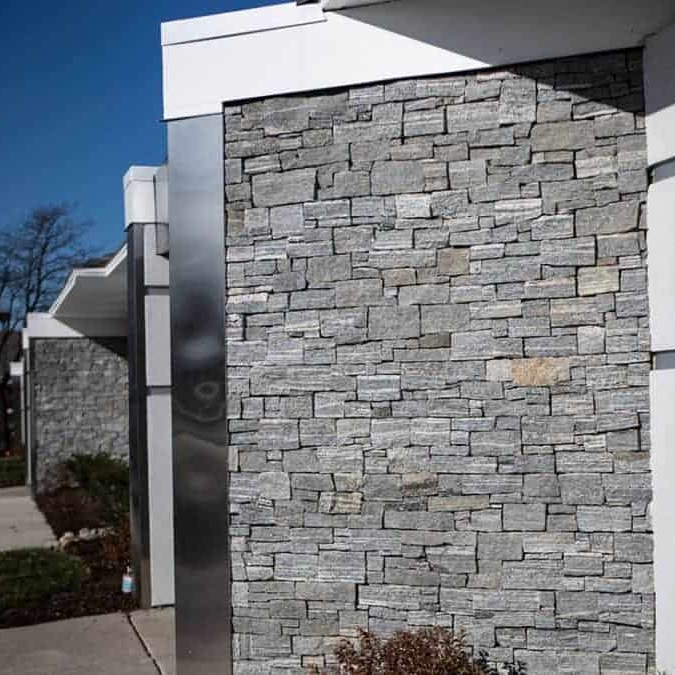 A modern building exterior featuring a textured stone wall alongside sleek metal accents and a clear blue sky.