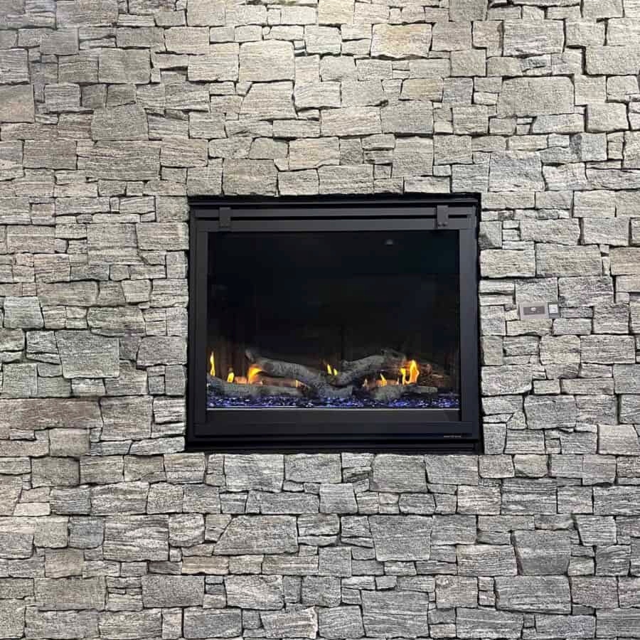 A modern fireplace embedded in a textured stone wall, showcasing glowing flames and a sleek black frame.