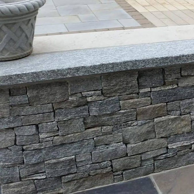 A stone wall featuring a mix of rectangular stones with a smooth granite top, accompanied by a decorative pot.
