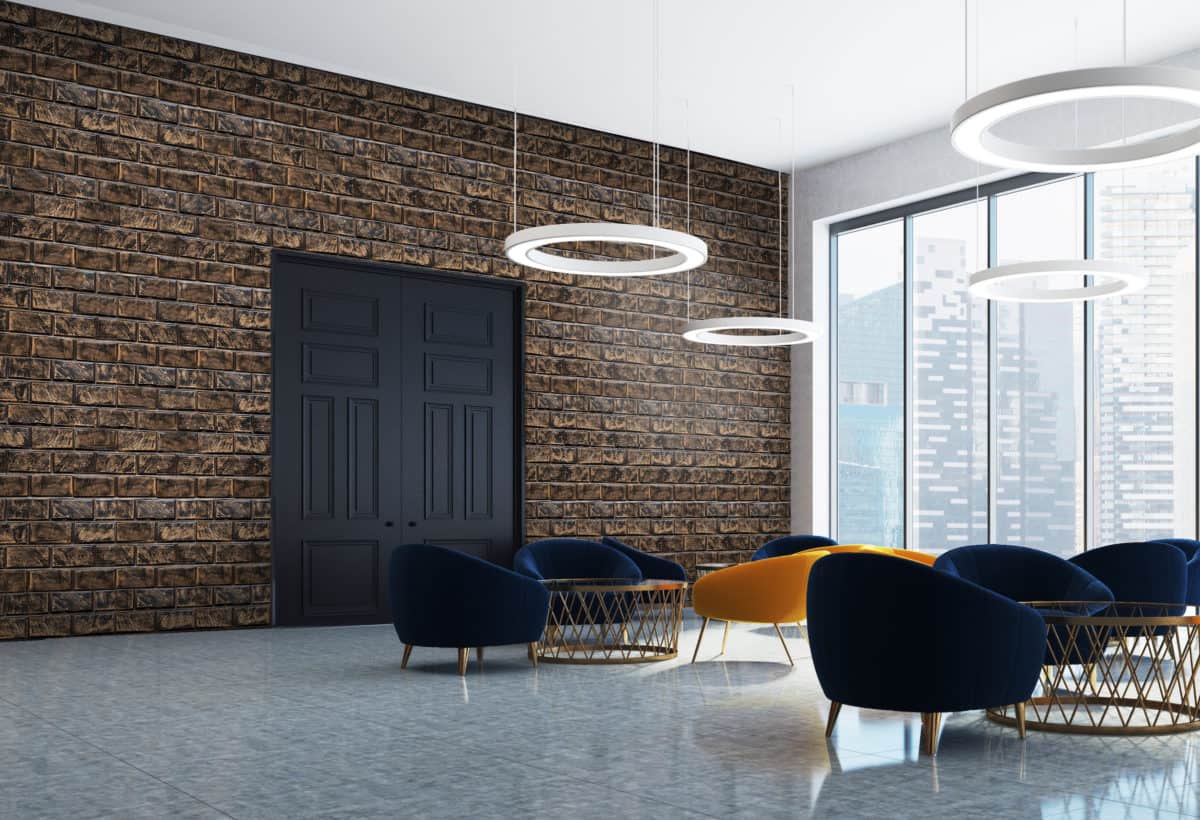 A modern interior featuring stylish blue and orange chairs, a stone wall, and circular light fixtures, with large windows providing a cityscape view.