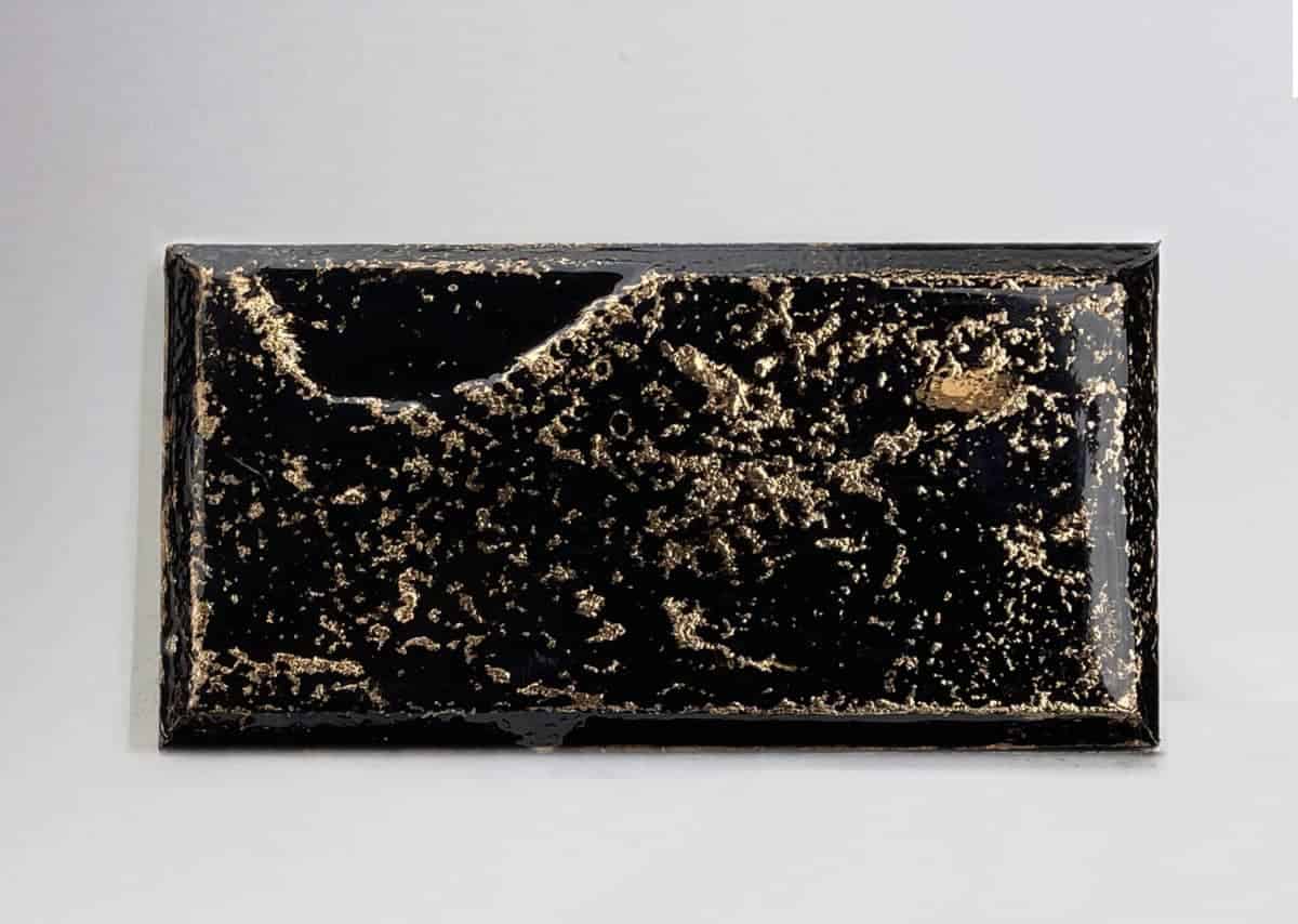 A rectangular black object with textured surface featuring gold and light brown patterns resembling abstract landscapes.