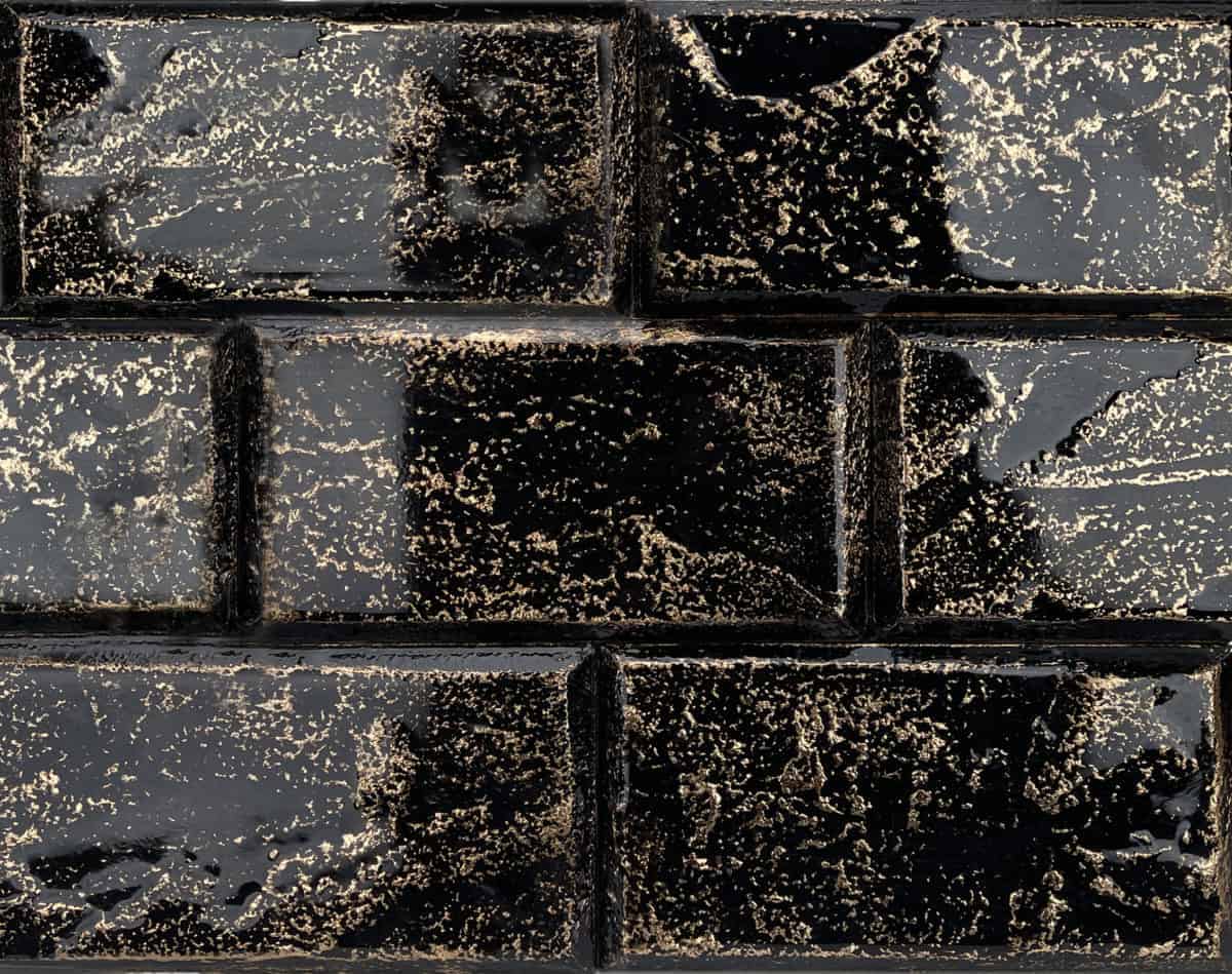 Glossy black brick wall with uneven surface, featuring a textured pattern and subtle wear marks.