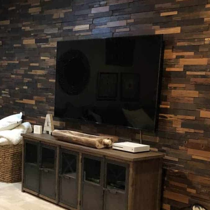 A modern living room featuring a large black TV mounted on a textured wooden wall, complemented by a rustic TV stand and decorative items.