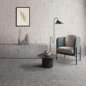 A minimalist interior scene featuring a gray floor, a modern chair, a small black table, and decorative elements including a plant artwork.