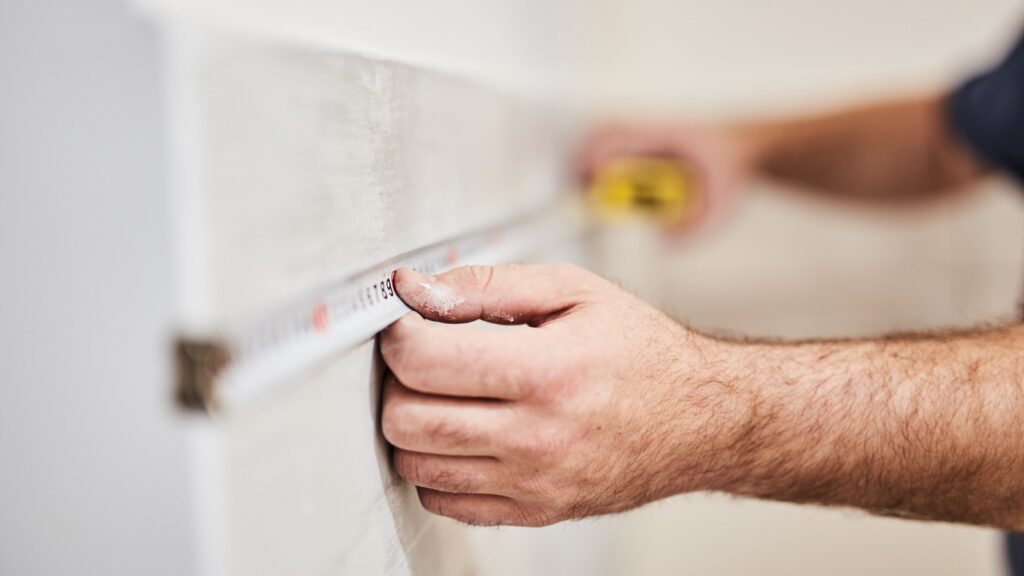 Close up of man's hands measuring the wall for a kitchen tile backsplash.