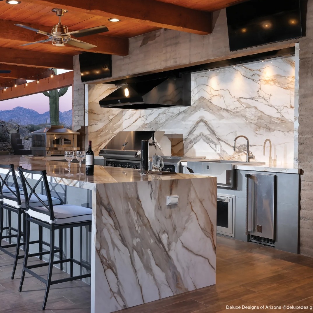 An elegant kitchen with marble surfaces, stainless steel appliances, and large windows showcasing a scenic outdoor view.