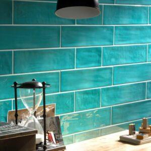 A turquoise tiled wall with a wooden table adorned with decor items, including an hourglass and various containers.